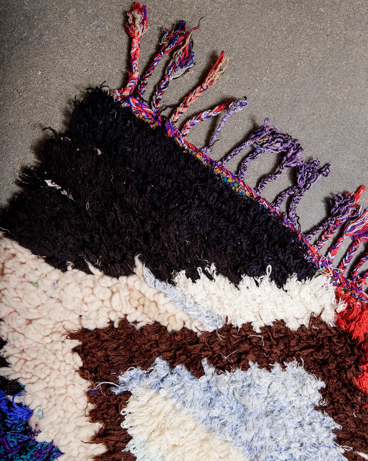 Cotton tassels on the the end of a runner rug made of wool and cotton laying on a concrete floor.
